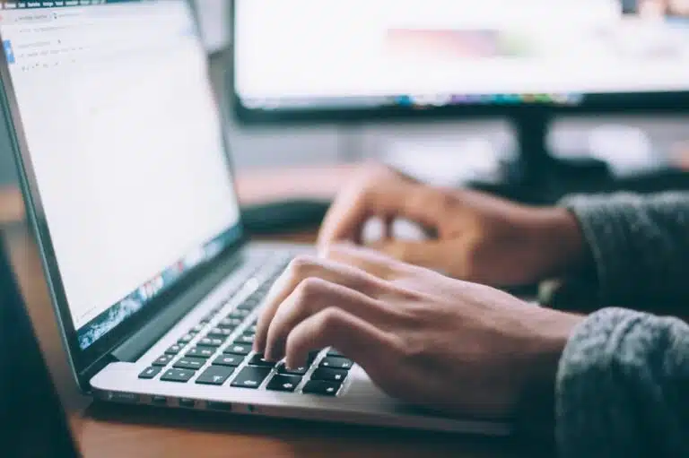 Nahaufnahme von Händen über der Tastatur eines Notebooks, auf dem Bildschirm ist zu erkennen, dass ein Schreibprogramm geöffnet ist